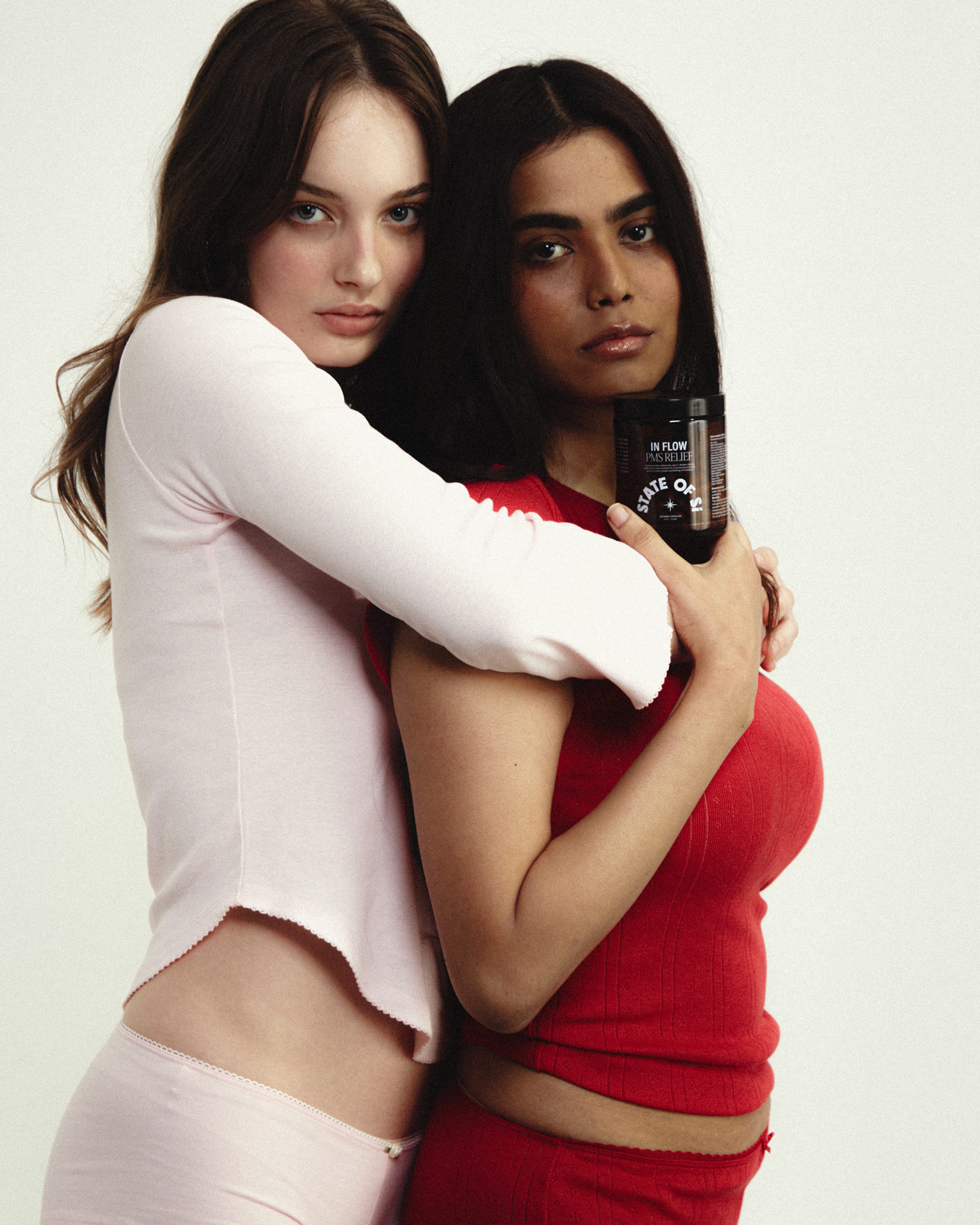 Two women holding State of Si, one in a white outfit and the other in a red outfit.