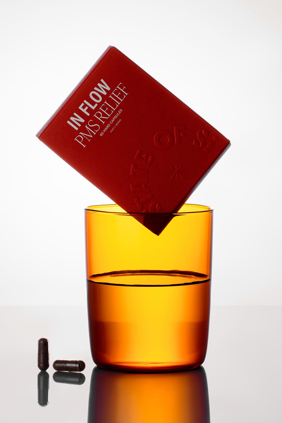 Orange glass with water, a red box labeled 'In Flow' and capsules on a reflective surface.